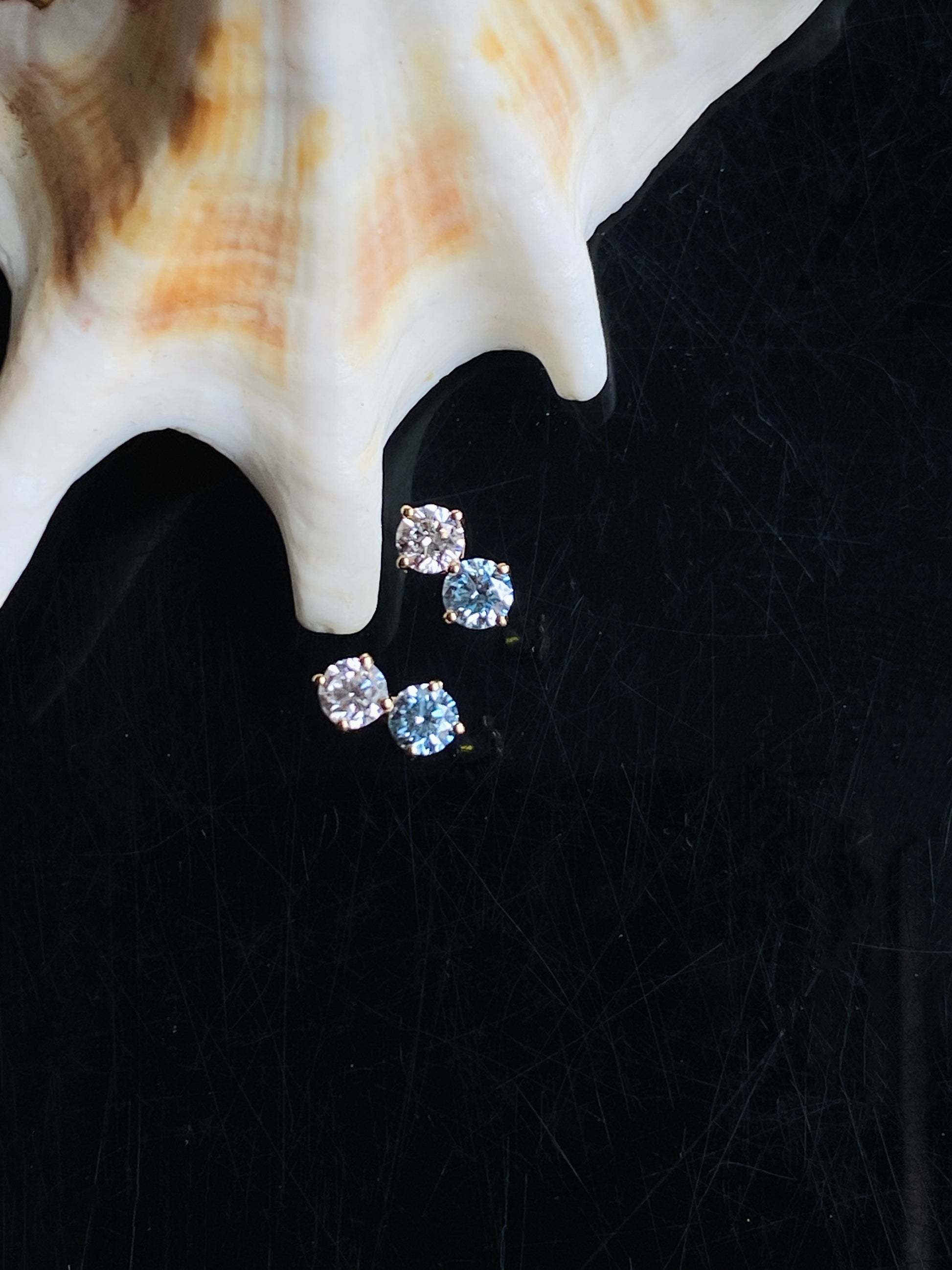 Three small crystal earrings on a black surface with a shell in the background
