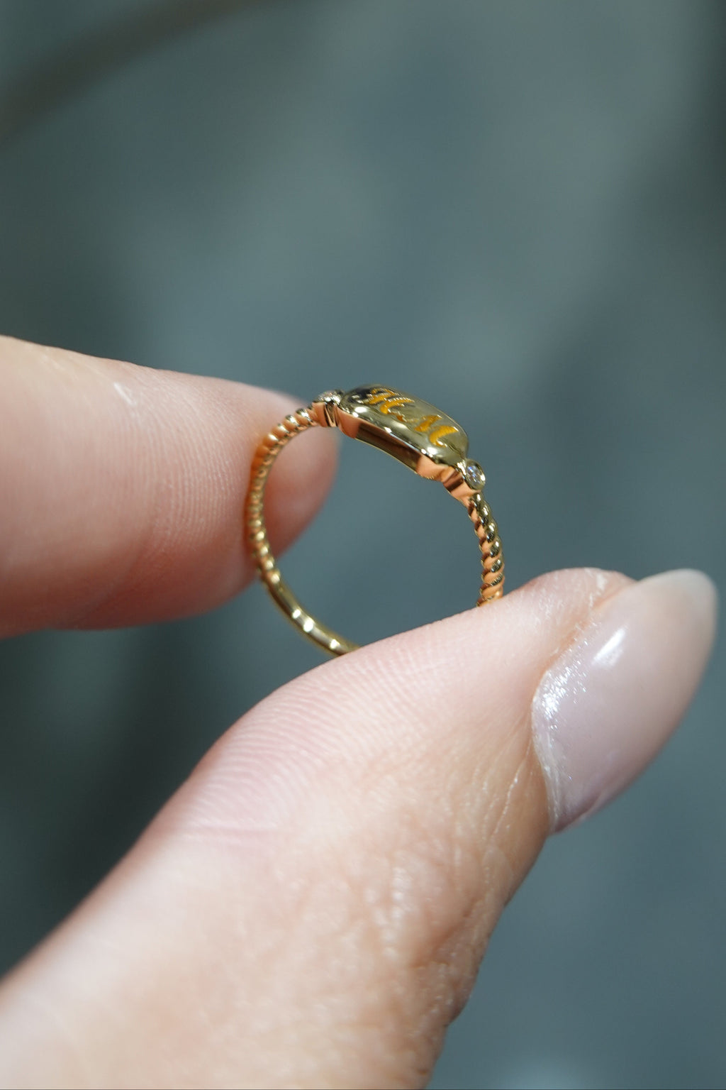 A close-up of a hand holding a delicate gold ring with a small oval yellow gemstone against a soft, blurred gray background.
